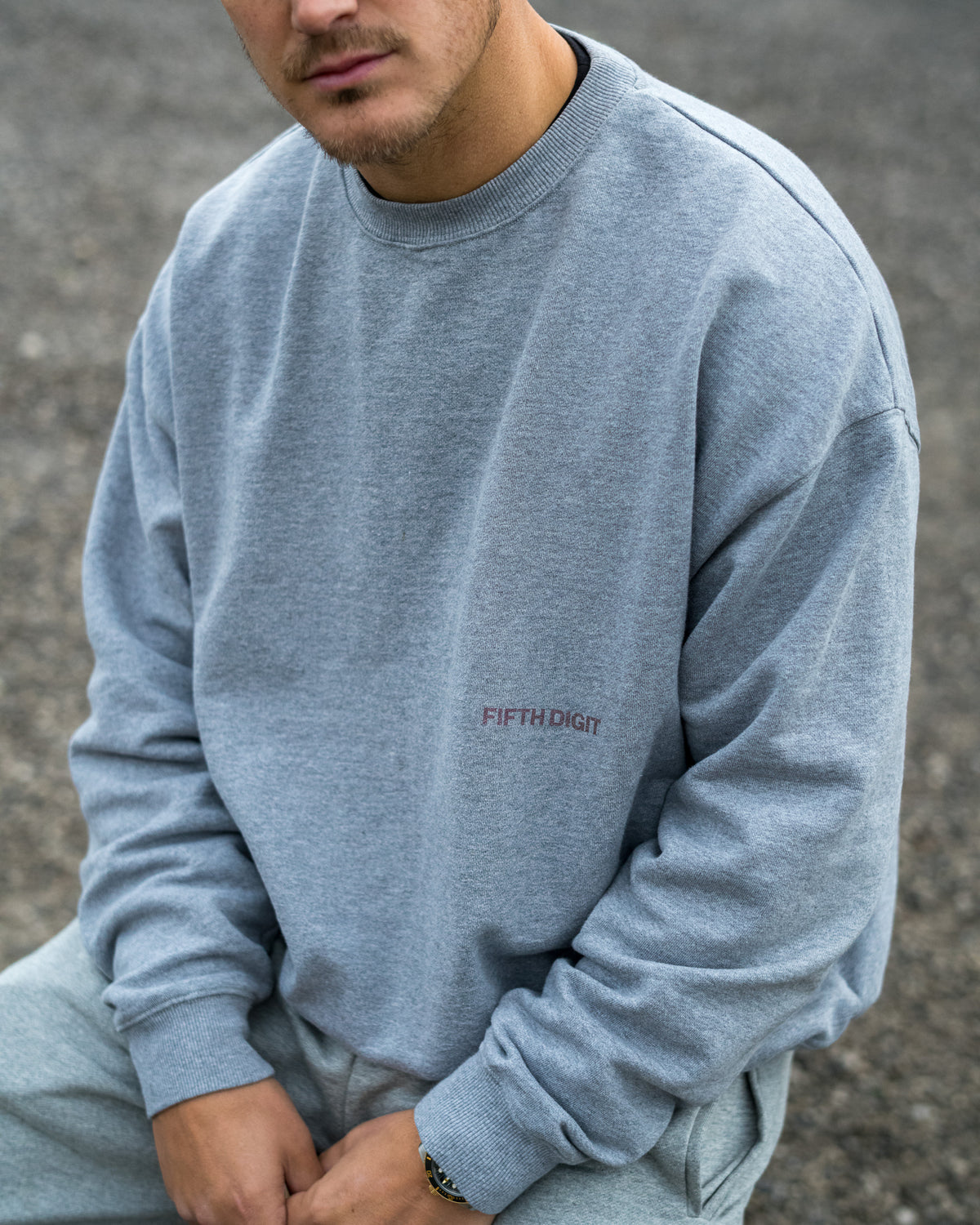 Fifth Digit Arch 460gsm crewneck in grey marl, seated, front view with the burgundy Fifth Digit chest print