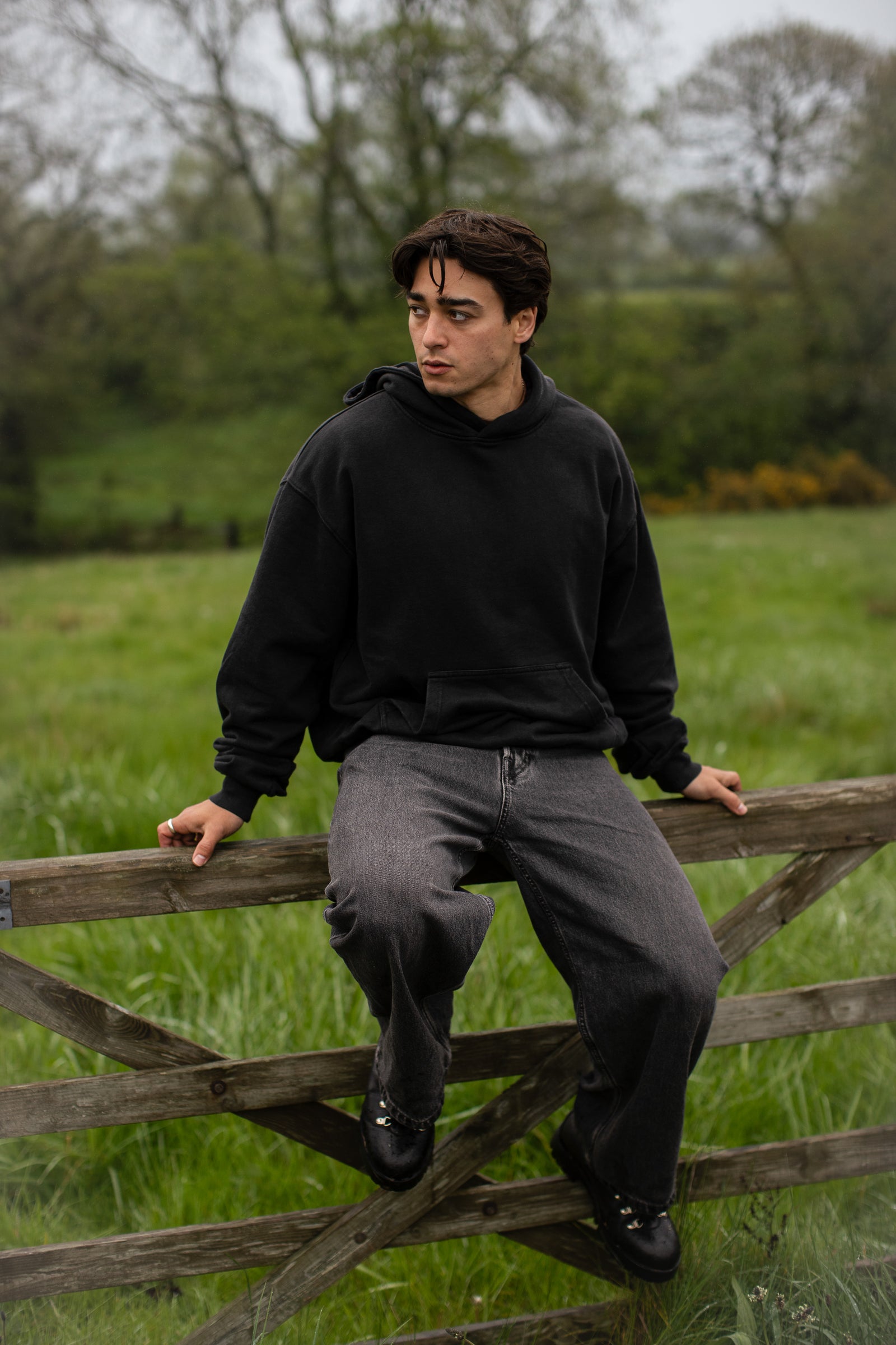 Fifth Digit Capsule 001 — figure in black tee pausing in long grass, head turned