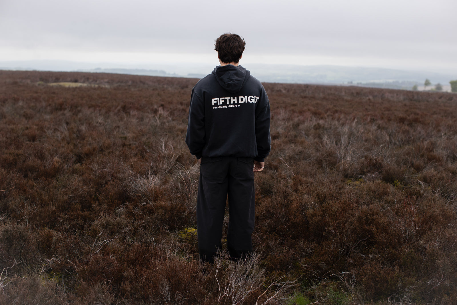 Fifth Digit Capsule 001 — back view of black hoodie on open moorland, FIFTH DIGIT genetically different print