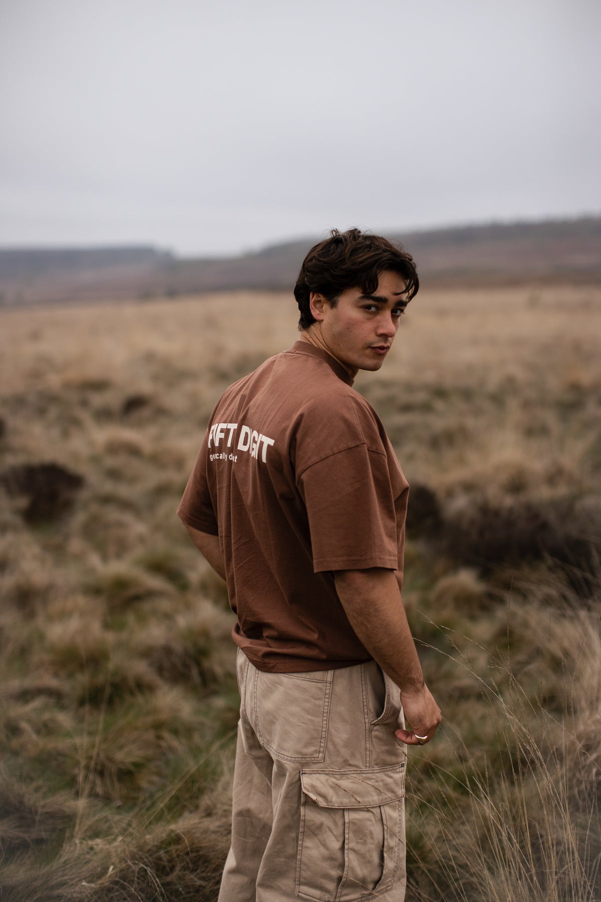 Fifth Digit Capsule 001 — figure in vintage brown Pressure tee on open moorland