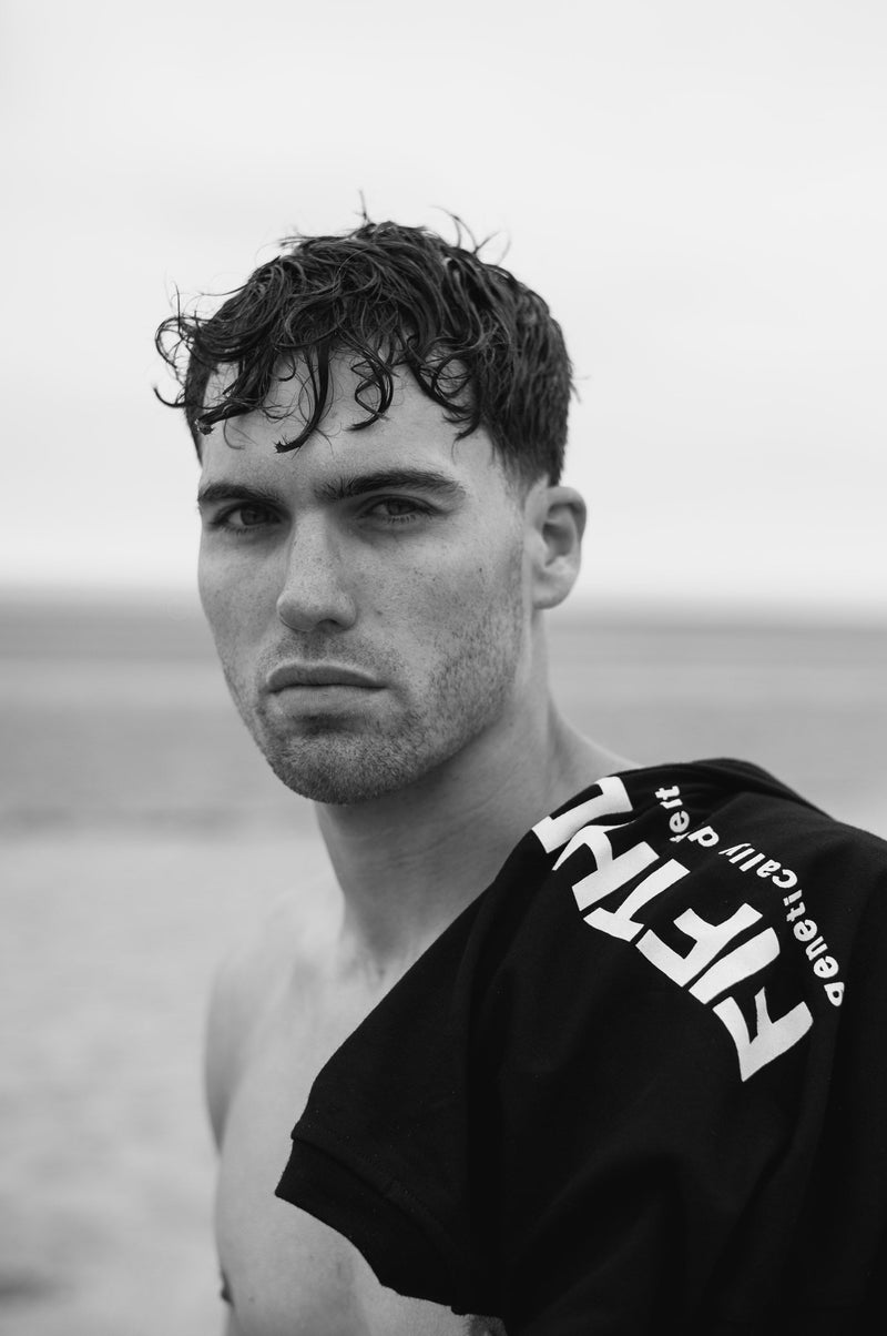 A close portrait of a man with wet hair, a black Fifth Digit tee over his shoulder with the print showing. Black and white.