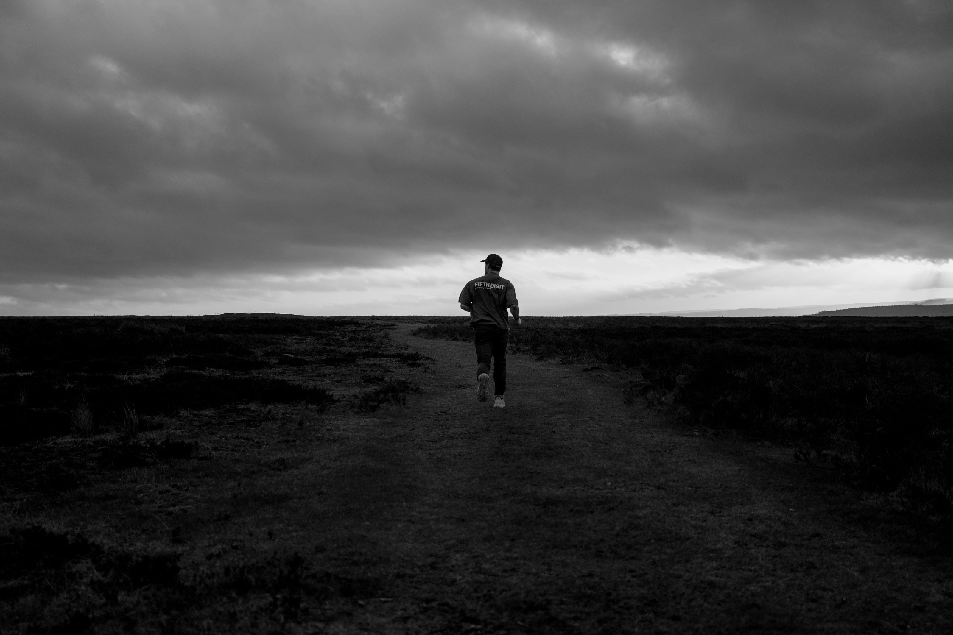 Model wearing Fifth Digit Identity T-Shirt walking across open moorland under overcast sky