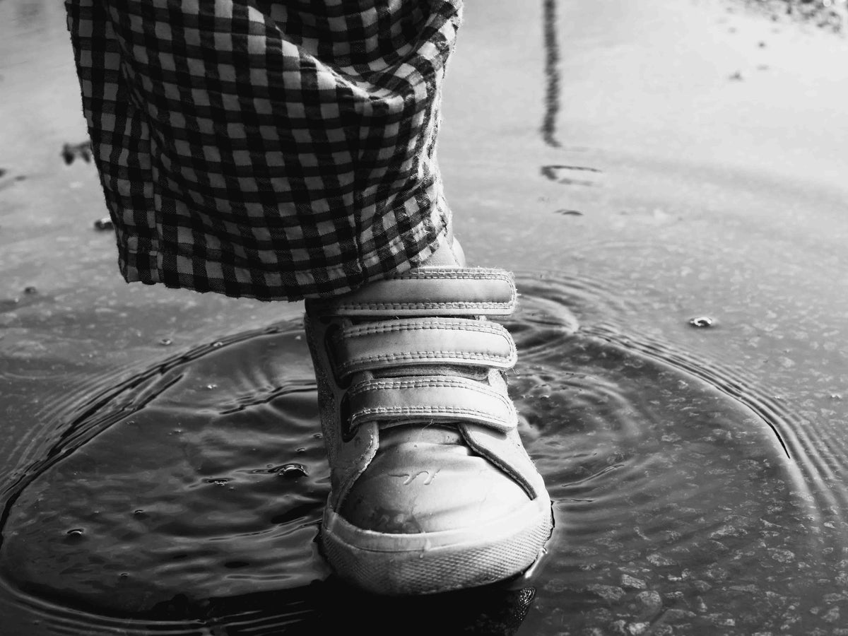 A small foot steps into a shallow puddle. Ripples spread across the surface. Black and white.