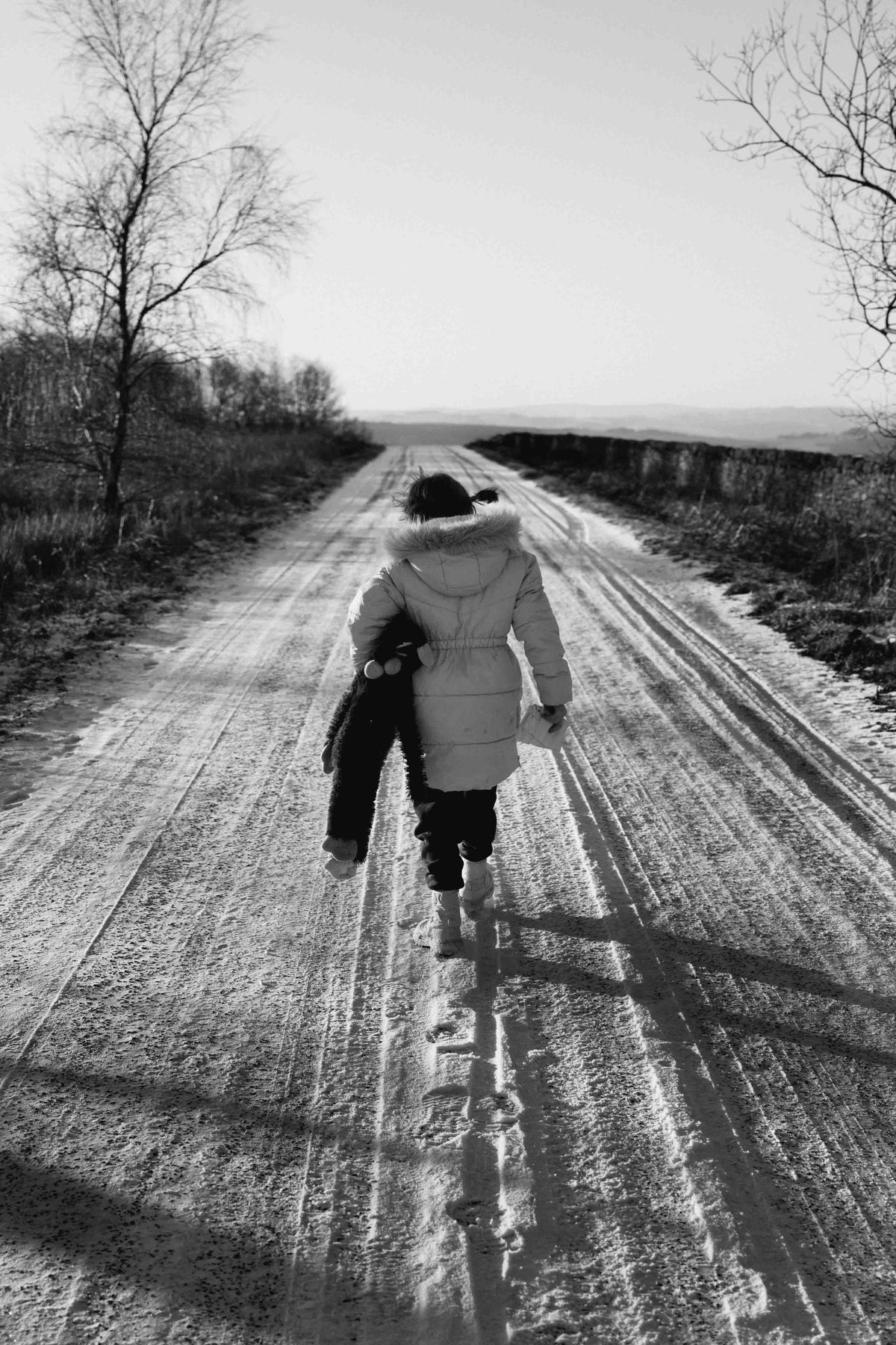 Back view of a figure on a snow-covered road. Long shadows on the ground. Black and white.