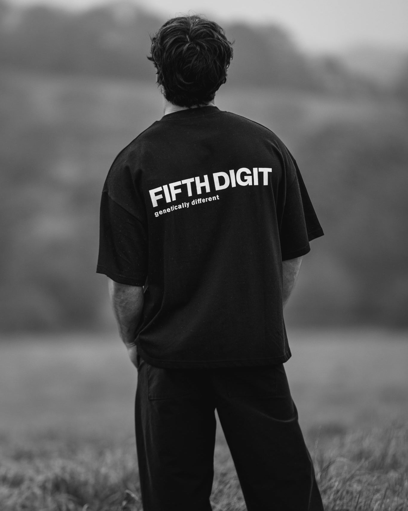 Fifth Digit Pressure tee back view. Genetically different back print visible. Black and white. Open countryside.
