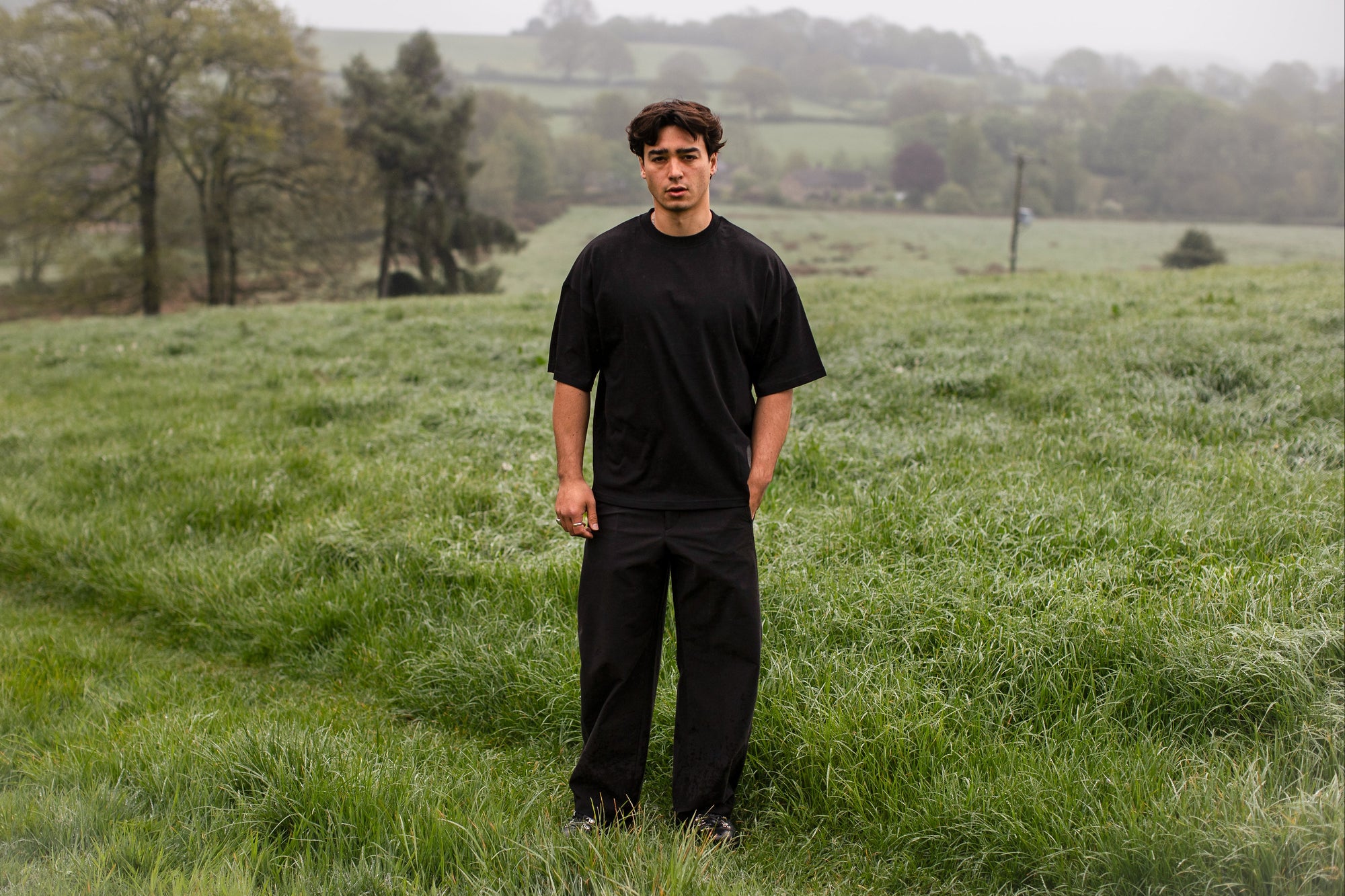 FIFTH DIGIT Pressure tee in black, worn by a model standing in a meadow. Oversized fit, 240gsm organic cotton.