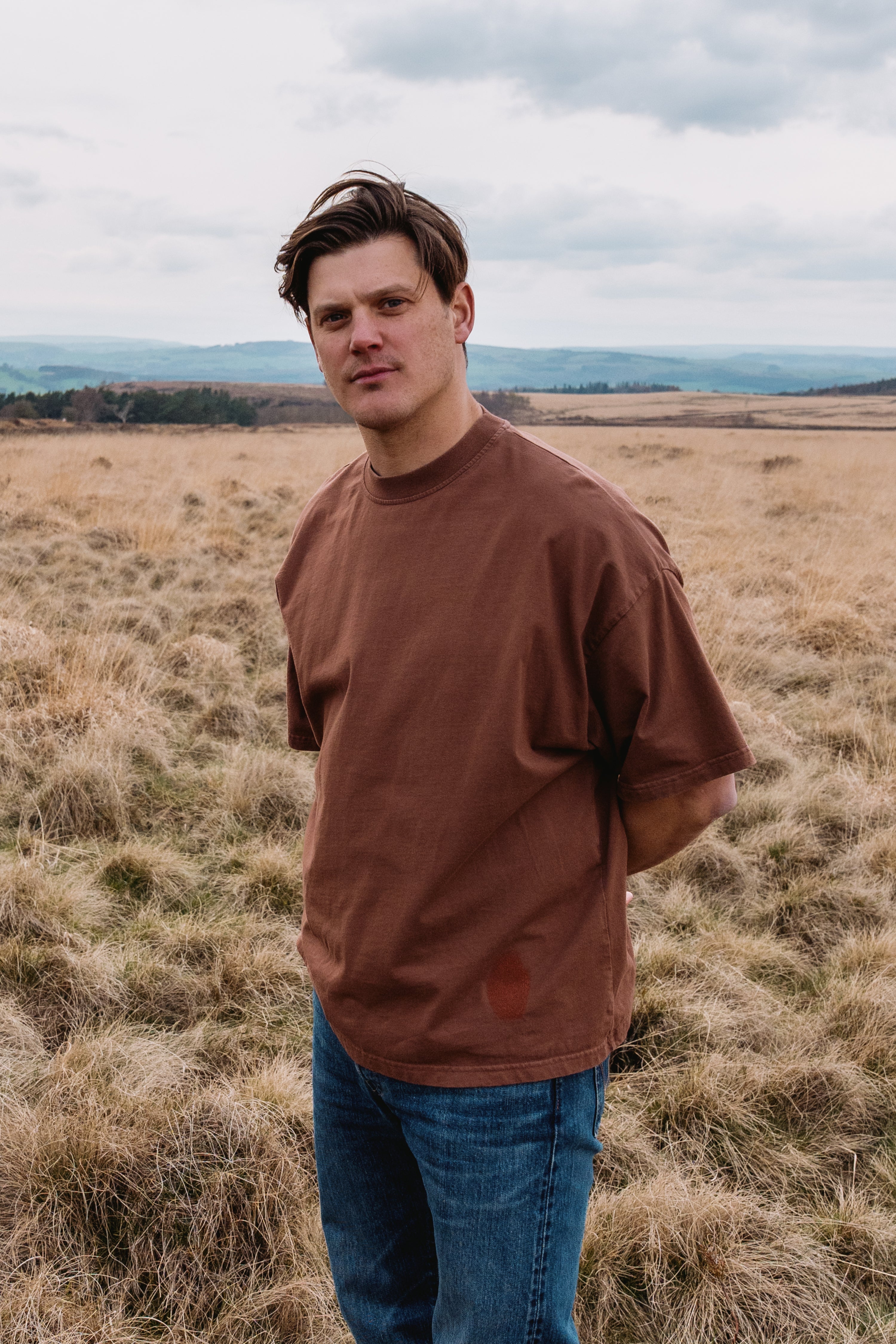 Model wearing vintage brown Identity T-Shirt in open landscape
